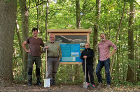 Vier Menschen vor einer Infotafel im Wald 