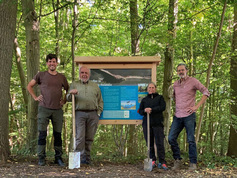 Vier Menschen vor einer Infotafel im Wald 